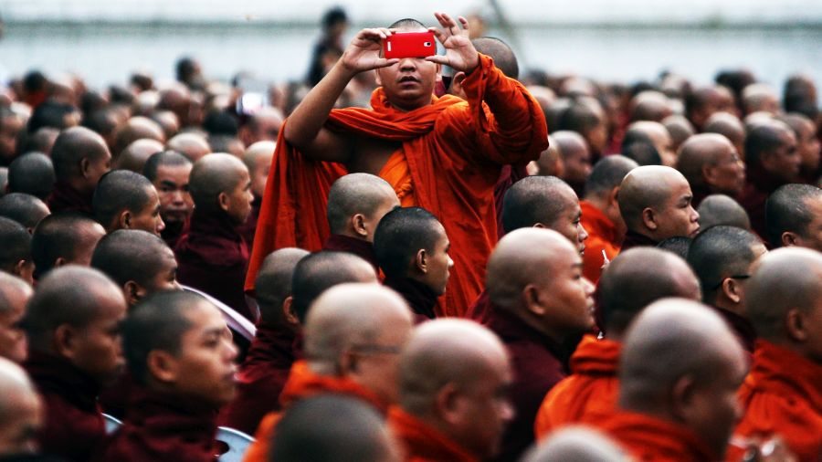 CORRECTION-ADDTTION A Buddhist monk takes a photo as he and other monks from Myanmar and Thailand are offered morning alms during the first ever Myanmar-Thailand friendship service in Mandalay on September 20, 2015. The mass joint alms event was organised by Thai and Myanmar Buddhist groups in what they say is a first and involves thousands of monks from both countries. / AFP / PHYO MG MG (Photo credit should read PHYO MG MG/AFP/Getty Images)