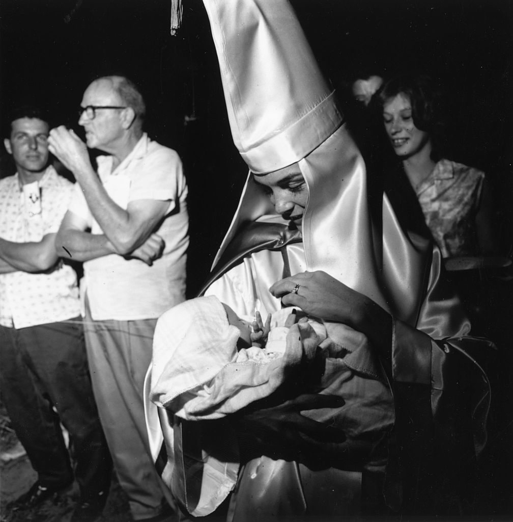 24th May 1965: A woman wearing the robes and hood of the American white supremecist organisation the Ku Klux Klan holding her baby at a klan meeting in Beaufort, South Carolina. (Photo by Harry Benson/Getty Images)